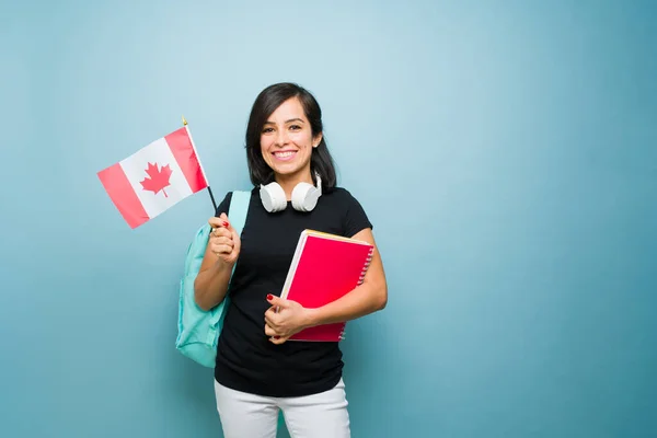 Attractive caucasian woman smiling carrying books and a backpack holding a canadian flag ready to learn English and studying abroad in Canada