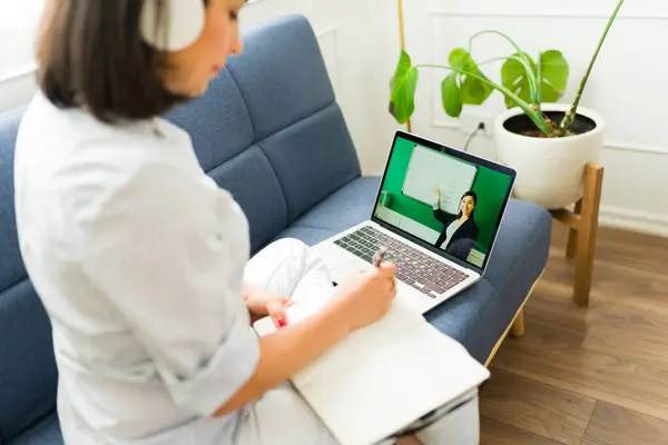 Rear view of a woman student sitting on the couch taking an English online class and a virtual course learning english