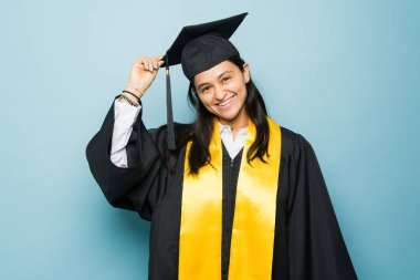 Meksikalı mutlu genç kadın üniversiteyi bitirdikten sonra üniversite diplomasını almak için gülümserken kep ve cübbesini takıyor.