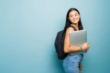 Kolej sınıfına yürürken yanında kitaplarını ve sırt çantasını taşıyan güzel Latin üniversiteli kadın kopya alanı reklamının yanında mutlu bir şekilde gülümsüyor.