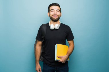 Okumak için kitap taşırken gülümseyen yakışıklı genç bir öğrenci ve üniversitedeyken sırt çantası.
