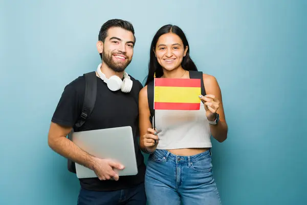 Latin young woman and happy man studying in university learning Spanish showing the Spain flag and looking happy