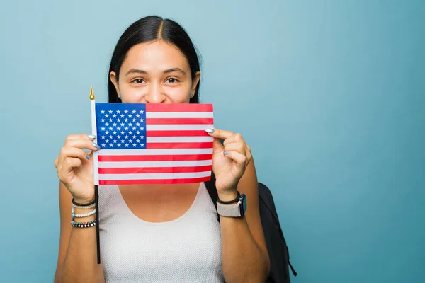 Portrait of a beautiful latin woman and student learning English and holding the United States flag looking happy