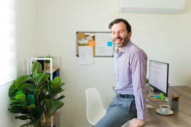Ofiste çalışırken gündelik kıyafetler giyen ve gülen neşeli, çekici bir latin adam bir girişimci gibi görünüyor.