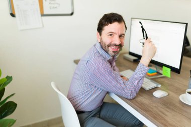 Ofis masasında otururken gülümseyen beyaz girişimci ve patron gözlüğünü takıp gülümsüyor.