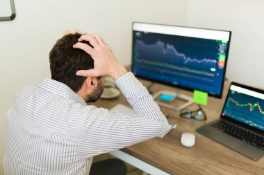 Stresli beyaz adam bağırıyor ve ofisteki bilgisayardaki borsaya bakarken yatırım için endişeleniyor.