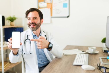 Gülümseyen Latin doktor, mutlu görünen bir tıbbi uygulama kullanarak akıllı telefonun boş ekranını işaret ediyor.