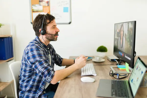 Side view of a sales representative with a headset sitting at the office desk and having a work video call
