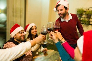Noel Baba şapkalı mutlu arkadaş grubu kadehlerini kaldırıyor. Noel tatilini akşam yemeğinde kutluyorlar.