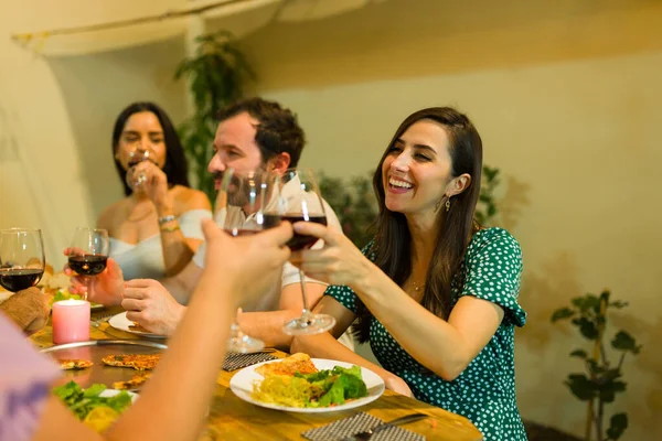 Smiling young women and men laughing having a toast drinking wine together after eating dinner during a social gathering