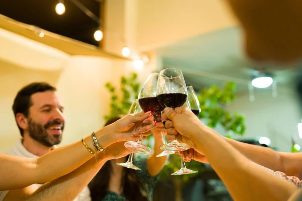 Close up of six people making a toast and having fun drinking wine and alcohol while laughing during a dinner with friends