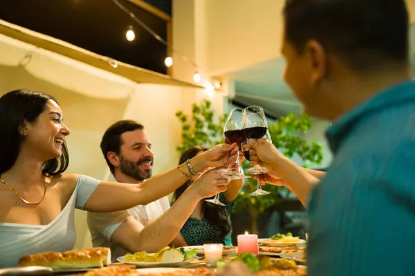 Group of six people making a toast and drinking wine at night during a dinner celebration with friends