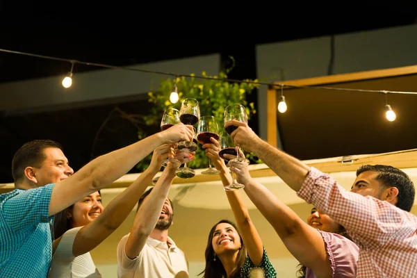 Happy group of friends smiling making a toast saying cheers drinking wine and having fun at night during a social gathering