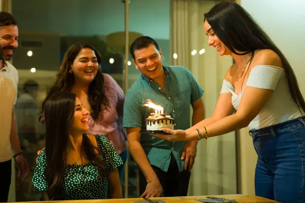 Cheerful group of friends bringing a surprise cake with candles to a happy young woman and celebrating