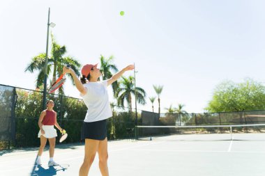 Aktif, mutlu, genç bir kadın tenis oynarken Latin bir antrenörden tenis dersi alıyor.