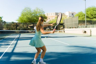 Çekici genç bir kadın spor yapıyor ve bir arkadaşıyla tenis oynarken forehand çalışıyor.