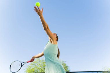 Latin sporcu genç bir kadın havaya tenis topu atıyor ve tenis maçı sırasında tenis oynamaya hazır.