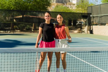 Tenis okulundayken tenis kortunda gülümseyen neşeli beyaz kız ve Latin kadın koç.