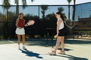 Profesyonel tenis koçu kadın, sahada beyaz bir kıza nasıl iyi tenis oynanacağını öğretiyor.