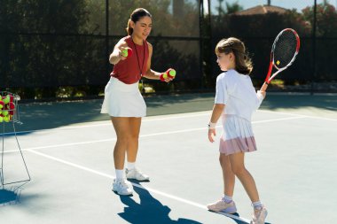 Güzel bir kadın tenis koçu tenis kortunda beyaz, sevimli bir beyaz kıza ders veriyor.