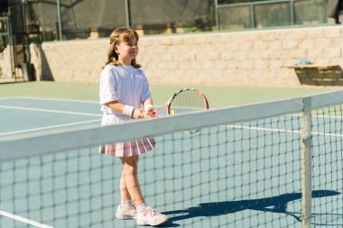 Tenis dersleri alırken ve raketle oyun oynarken gülümseyen mutlu beyaz kız.