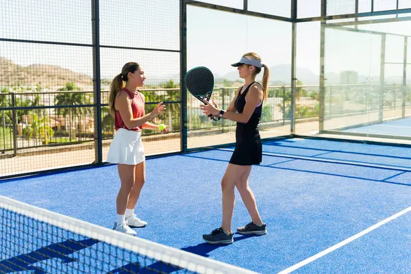 Happy woman trainer with a caucasian woman  talking about padel during a tennis lesson outdoors having fun