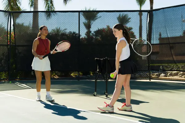 Professional tennis coach woman teaching how to do a good tennis serve to a caucasian teen girl on the court