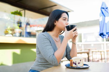 Çekici İspanyol genç kadın kahve ya da kapuçino içiyor ve kahvecide dinlenirken hamur işi yiyor. 