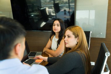 Günlük giysiler içinde iki iş kadını bir müşteriyle konuşuyor ve bir toplantı odasında proje sunuyorlar.