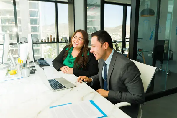 Two businesspeople talking and laughing in an office while doing some work together
