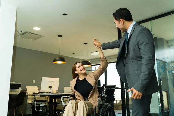Happy disabled woman in a wheelchair looking happy and giving a high five to a coworker