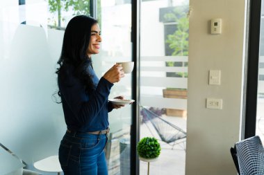 Mutlu bir ofis çalışanı iş molasında kahve içip gülümsüyor.