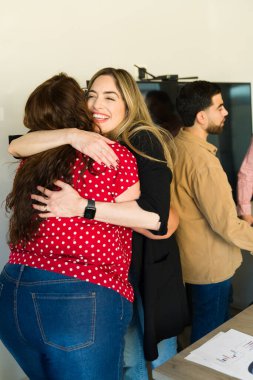 İki kadın iş arkadaşı birbirlerine sarılıyor ve toplantı odasında mutlu görünüyorlar.