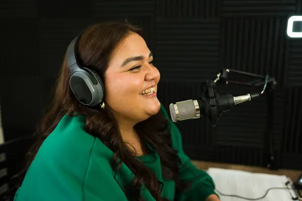 Excited latin woman radio host smiling looking happy while doing a talk show and podcast in the recording studio