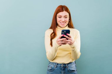 Akıllı telefonla mesajlaşırken gülümseyen ve online sosyal medya kullanan mutlu kızıl saçlı kadın.