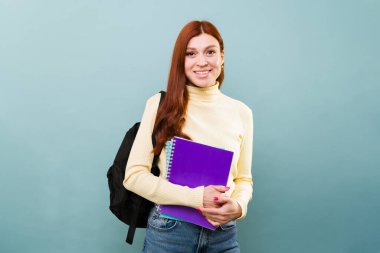 Kızıl saçlı, çekici bir kızın portresi. Sırt çantasıyla üniversiteye giderken gülümsüyor.