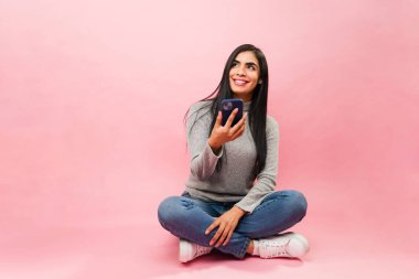 Güzel Meksikalı kadın gülümseyip mesajlaşırken ya da sosyal medyayı pembe arka planda kullanırken düşünüyor.