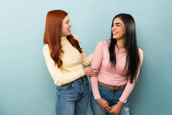 Excited red hair woman and latin female, best friends laughing looking very happy while joking together