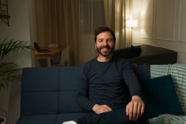 Mutlu beyaz adam gülümsüyor. Oturma odasındaki kanepede dinleniyor. Geceleri evinin tadını çıkarıyor.