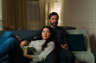 Çekici evli çift kanepede dinleniyor. Oturma odasında patlamış mısır yerken televizyonda film izliyorlar.