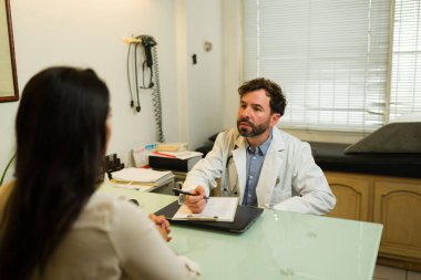 Sağlık ocağında sağlık kontrolünden sonra kadın bir hastayla alternatif tıp hakkında konuşan yakışıklı bir doktor.