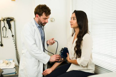 Muayene sırasında hasta bir kadının kan basıncını ölçmek için baumanometreyi kullanan yakışıklı İspanyol doktor.