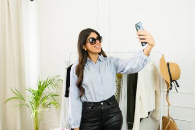 Güneş gözlüklü, şık bir genç kadın elbise mağazasında selfie çekiyor.