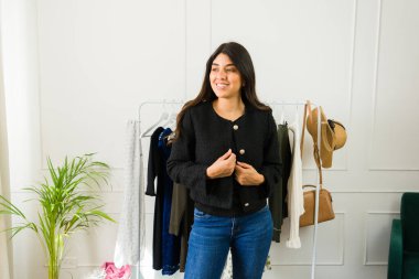 Neşeli genç bir kadın butikte kıyafet seçiyor, mutlu bir ifadeyle.