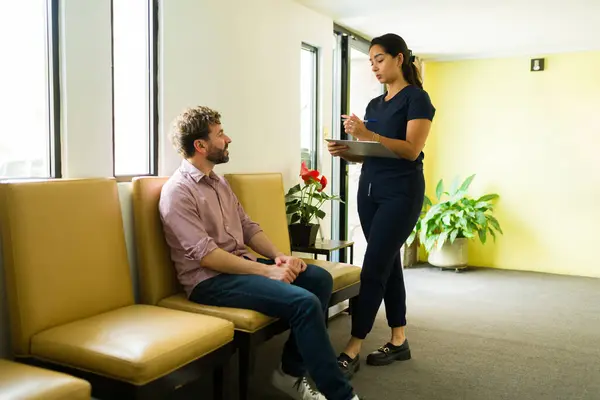 Latin happy nurse asking medical personal information and symptoms to a male patient in the waiting room of the wellness clinic