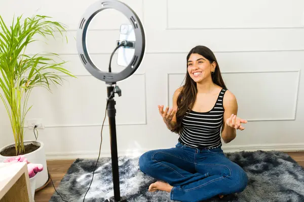 Gülümseyen kadın vlogger, rahat bir odada halka ışığıyla video kaydediyor.