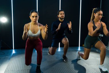 Üç odaklanmış yetişkin grup fitness kursu sırasında enerjik bir çömelme egzersizi yapıyor.