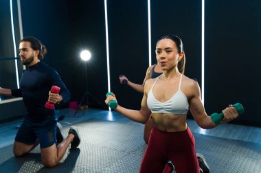 Bir beden dersine odaklanmış katılımcılar canlı ışıkların altında ağırlık kaldırıyorlar.