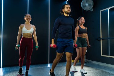 Spor salonunda halterleri tutan üç kişi fitness kursuna gidiyor.