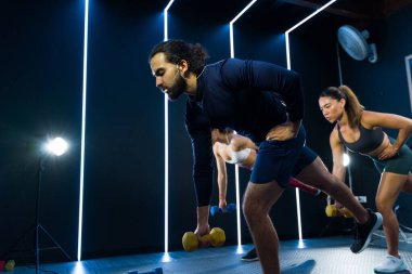 Çağdaş bir spor salonunda dinamik egzersiz dersinde ağırlık kaldıran odaklanmış bir grup sporcu